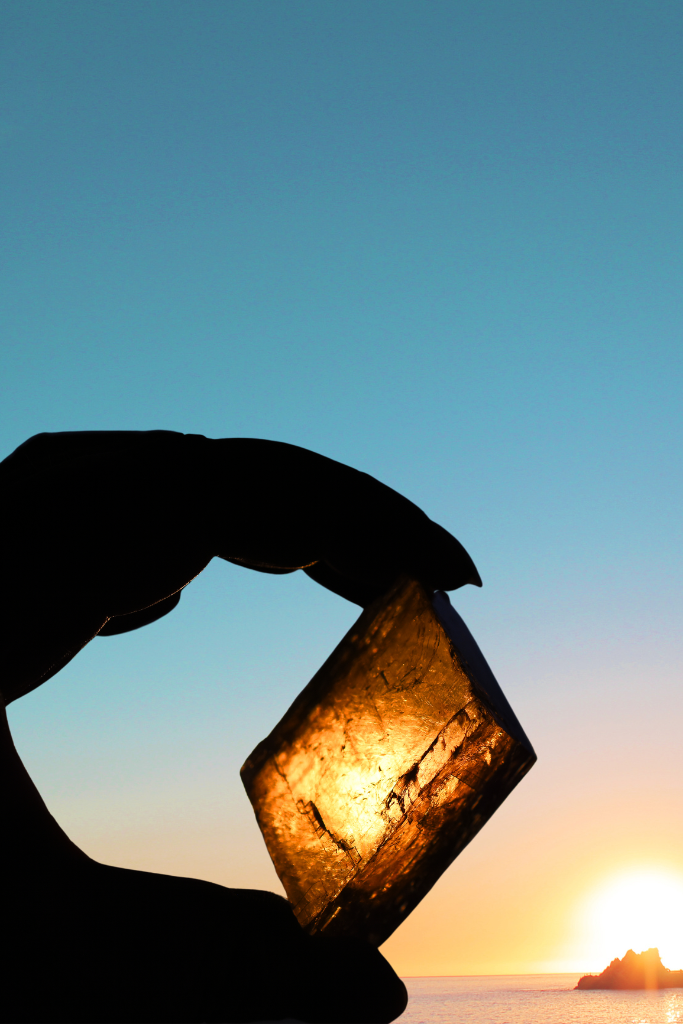 Photo of a hand holding up a piece of honey calcite in front of a sunset. 