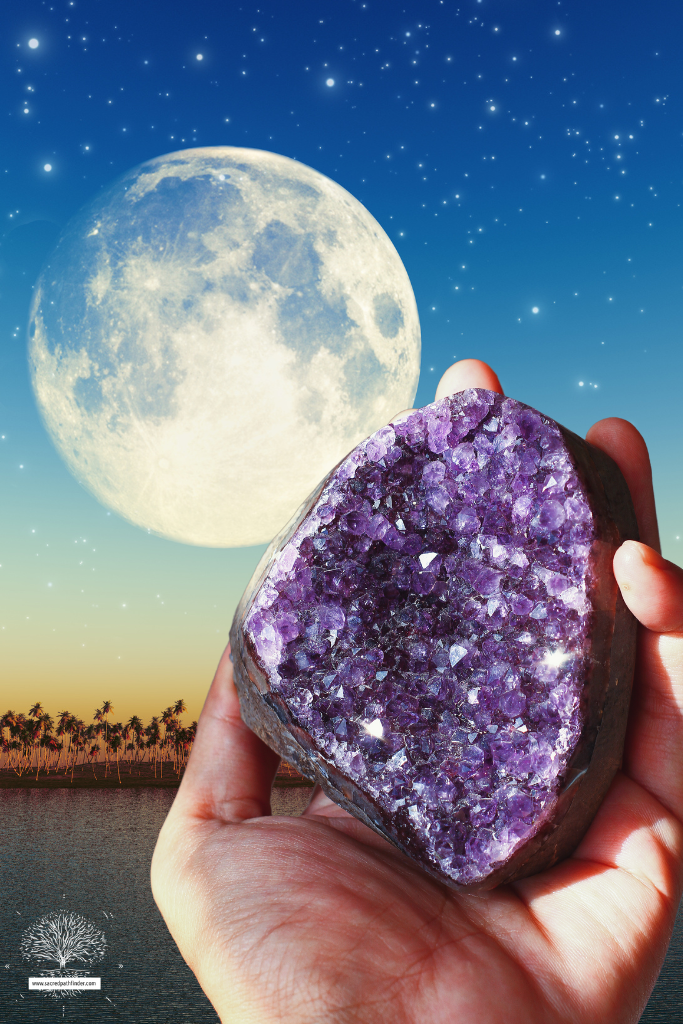 Photo of a hand holding a raw crystal in front of a full moon background.