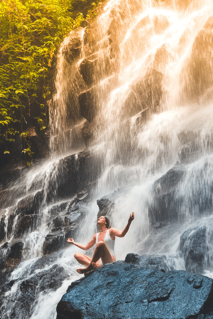 Photo of a woman meditating in front of a beautiful waterfall. 