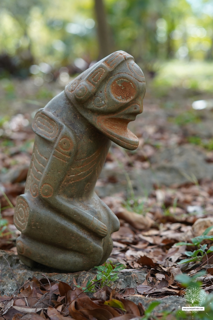 Photo of a small taino statue in the forest on the ground. 