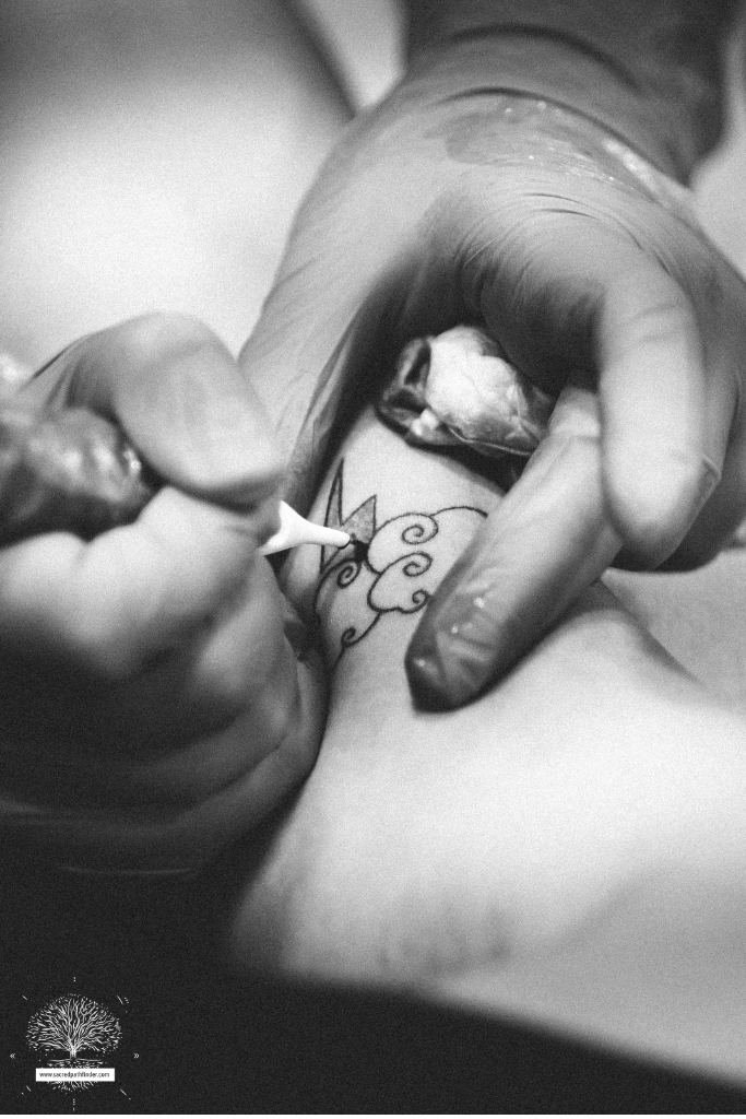 Black and white photo of a body being tattooed with a poke method.