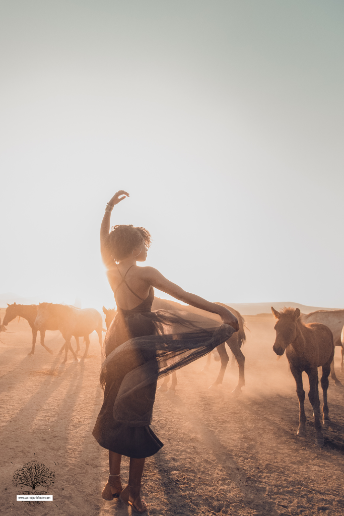 Photo of a woman dancing with a herd of horses around her. You can only see the back of her. 