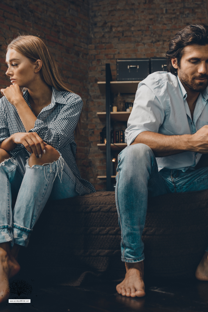 Photo of a couple on the edge of their bed. The man is looking at his phone and the woman looks sad. 