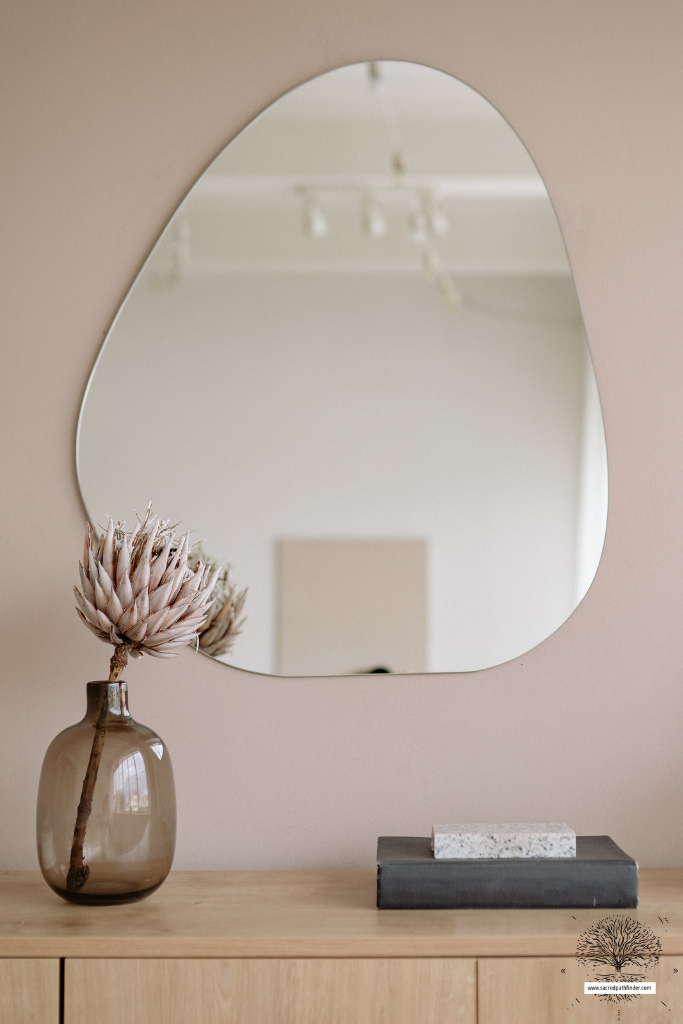 Closeup photo of a media console with a mirror over it. There is a vase with a flower and books on the console. 