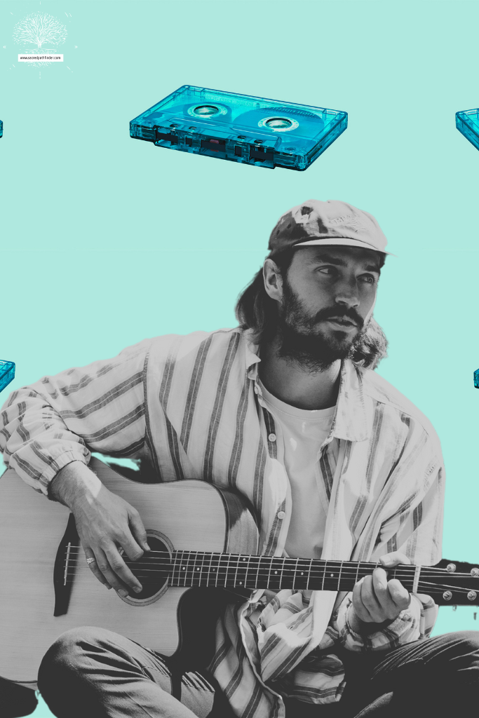 Black and white photo of a man playing the guitar. The background is of blue colored cassette tapes. 