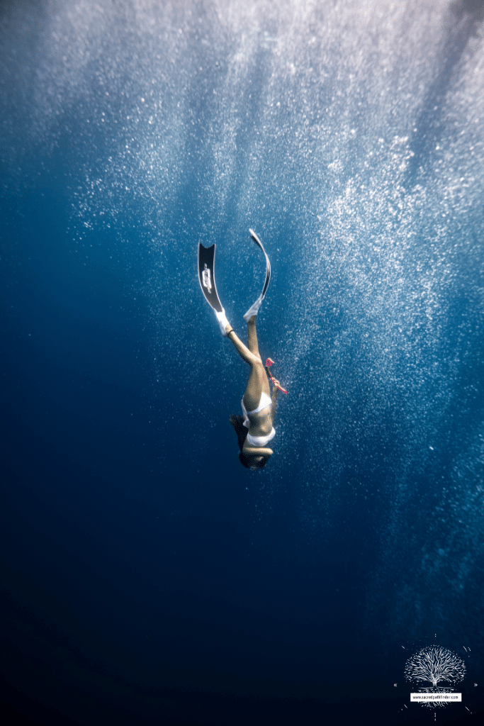 Photo of a woman diving in the ocean. She has swim fins on.